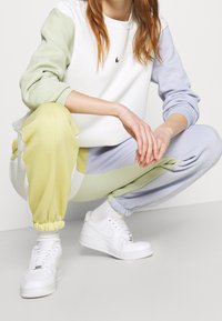 Ensemble de vêtement de détente comprenant un sweat-shirt blanc avec des manches vertes et lavande, un pantalon de survêtement pastel assorti avec des blocs de couleur, et des baskets blanches.