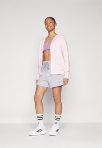 Kerge roosa biki ja valgete detailidega kapuutsiga jope, kombineeritud lilla spordibrassi, hallide lühikesed pükste ja valgete mustrıitega spordijalanõudega.