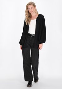 Cardigan nero lavorato a maglia con apertura frontale, maniche lunghe e texture a costine. Abbinato a pantaloni neri a vita alta e stivali neri con lacci.