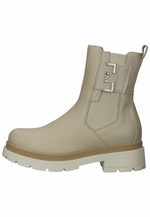 Bota de tobillo de cuero beige con una suela blanca gruesa, paneles elásticos laterales y un detalle de hebilla plateada. Textura suave y punta redondeada.