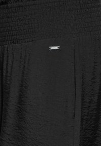 Svarta tygshorts med smockad midja, mjuk textur och en liten metallisk logotyp. Enkelt och strömlinjeformat design.