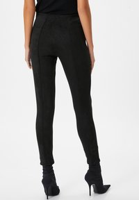 Leggings de ante sintético negro con cintura alta, ajuste slim y textura suave. Presentan costuras centrales y se combinan con botas de tacón alto negras.