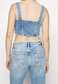 Niebieska jeansowa bluzka o kroju cropped z szerokimi ramiączkami, z kwadratowym dekoltem i surowym wykończeniem. Połączona z jasnoniebieskimi spodniami z wysokim stanem i tylnymi kieszeniami.