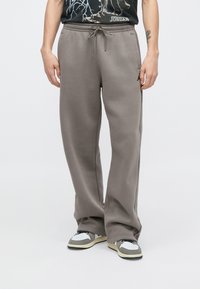 Graue Jogginghose mit lockerem Schnitt, elastischem Bund mit Kordelzug und seitlichen Taschen. Getragen mit grauen und weißen Turnschuhen.