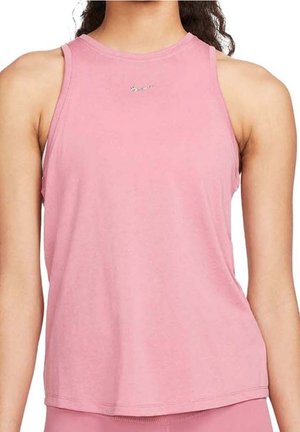 Kobieta ubrana w różowy, bezrękawnik z małym, srebrnym logo umieszczonym na środku przy dekolcie, stojąca na tle gładkiej białej ściany.