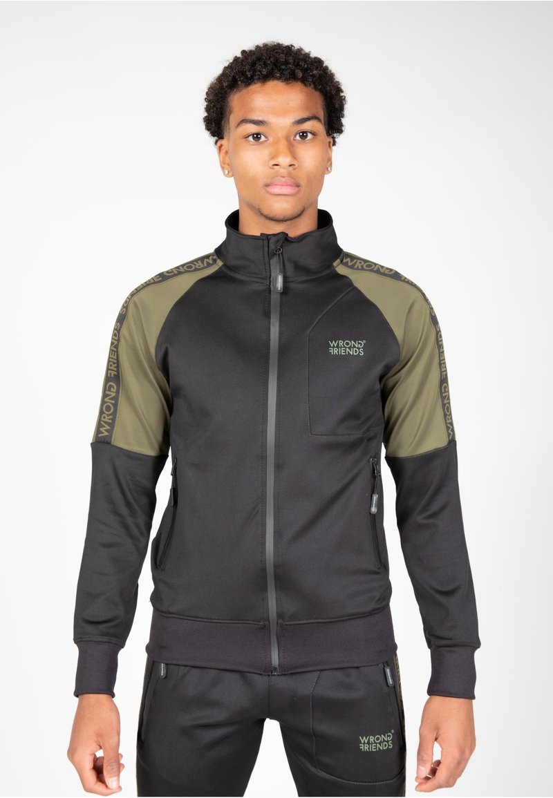 Giacca nera con zip, dotata di pannelli sulle spalle color verde oliva, logo "WRONG FRIENDS" sul petto e sulle maniche, realizzata in tessuto testurizzato e flessibile.