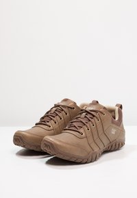Braune synthetische Schuhe mit strukturierter Oberfläche, runden Zehen und gepolsterten Sohlen. Verfügt über geflochtene Schnürsenkel und Branding an der Seite.