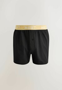 Boxers pour hommes noirs avec une ceinture élastique jaune arborant le logo blanc "NEXT" répété et une braguette avant à bouton unique.