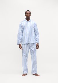 Costum de pijama raiat, format dintr-o cămașă cu guler și nasturi și pantaloni asortați. Fabricat dintr-un material ușor, cu dungi albe, albastre și albastre deschise.