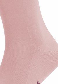 Chaussette en coton rose clair avec une texture côtelée, un design lisse et sans motifs visibles. Comprend un logo de marque violet foncé près de la zone des orteils.
