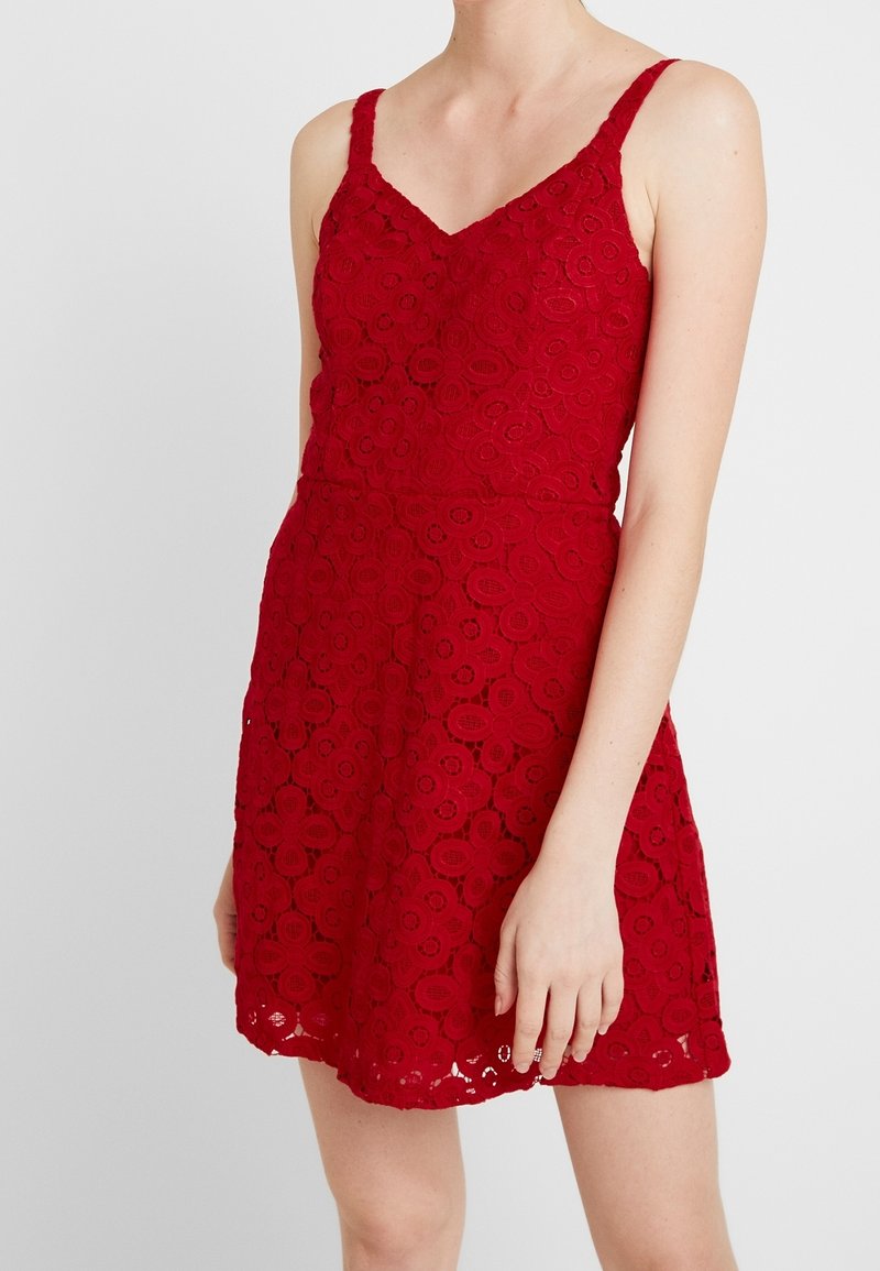 Rode kanten jurk met een getailleerd lijfje, een V-hals en dunne bandjes, versierd met bloemmotieven en een uitlopende rok.