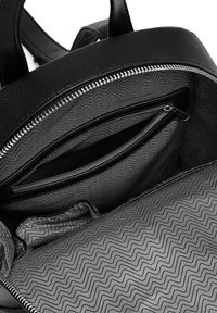 Schwarzer Leder-Rucksackinnenraum mit einem gemusterten Futter und Zickzacktextur, einer Reißverschlusstasche und einer zusätzlichen Einschubtasche.