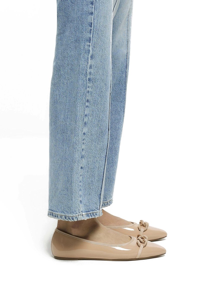 Ballerines patinées nudes avec un détail de nœud au niveau des orteils, portées avec des jeans en denim droit bleu clair avec des ourlets effilochés.