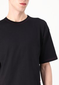 Czarny T-shirt wykonany z bawełny, z okrągłym dekoltem, krótkimi rękawami oraz kontrastowym różowym szwem wzdłuż kołnierza i rękawów.