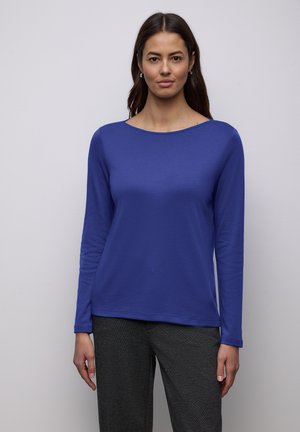 Long-sleeve top in solid royal blue fabric with a wide neckline and smooth texture, paired with dark gray pants.