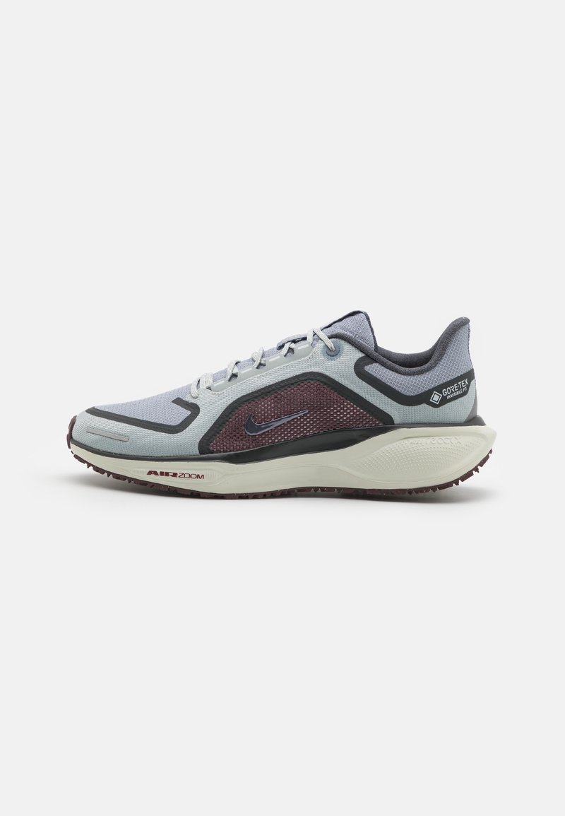 Chaussure de course gris clair avec un design en mesh, accents violets, et une semelle noire texturée. Dispose des marques GORE-TEX et "AIR ZOOM".