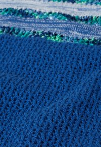 Blauwe gebreide stof met een gestructureerd patroon, met verticale ribbels en hier en daar lichte blauwe en groene garen door elkaar.