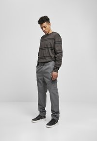 Langarm donkergrijs gestreept shirt, grijze cargobroeken met elastische tailleband en zwarte sneakers met witte zolen, gepositioneerd tegen een effen achtergrond.