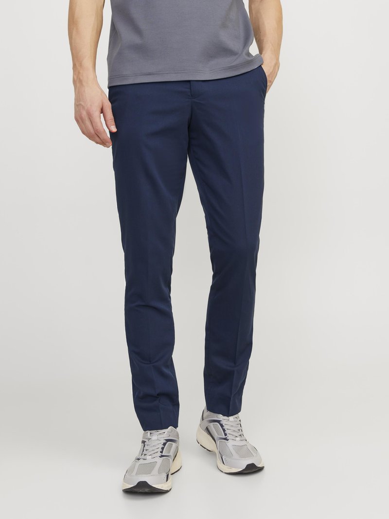 Marineblaue Slim-Fit-Hose aus glattem Stoff, mit Seitentaschen und einem schlichten Design, kombiniert mit grauen Sportschuhen.