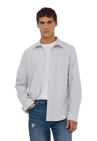 Camicia button-up con strisce verticali blu e bianche, maniche lunghe, taschino sul petto e vestibilità comoda, indossata sopra una maglietta bianca.