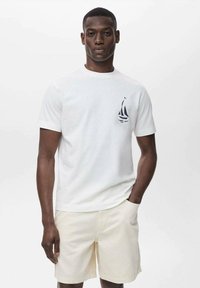 White cotton t-shirt with a crew neck, featuring a navy sailboat graphic on the chest, paired with beige shorts. Smooth texture.
