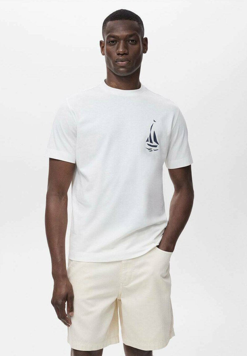 White cotton t-shirt with a crew neck, featuring a navy sailboat graphic on the chest, paired with beige shorts. Smooth texture.