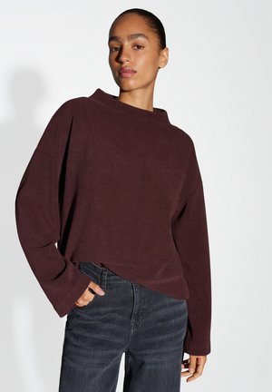 Bordeaux lange mouwen top met een hoge hals, zachte textuur, ontspannen pasvorm en verlaagde schouders, gecombineerd met donkere jeans.