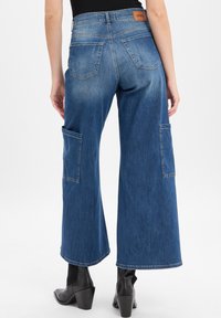 Wide-leg denim jeans in faded blue with a smooth texture, featuring two side pockets and a leather brand patch on the waistband.