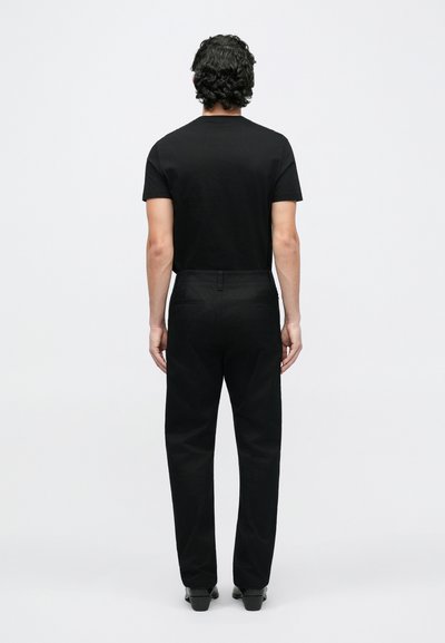 Fekete rövid ujjú póló és fekete nadrág hátsó nézetből. Az anyag simának tűnik, testhezálló szabású, minimális részletezéssel.
