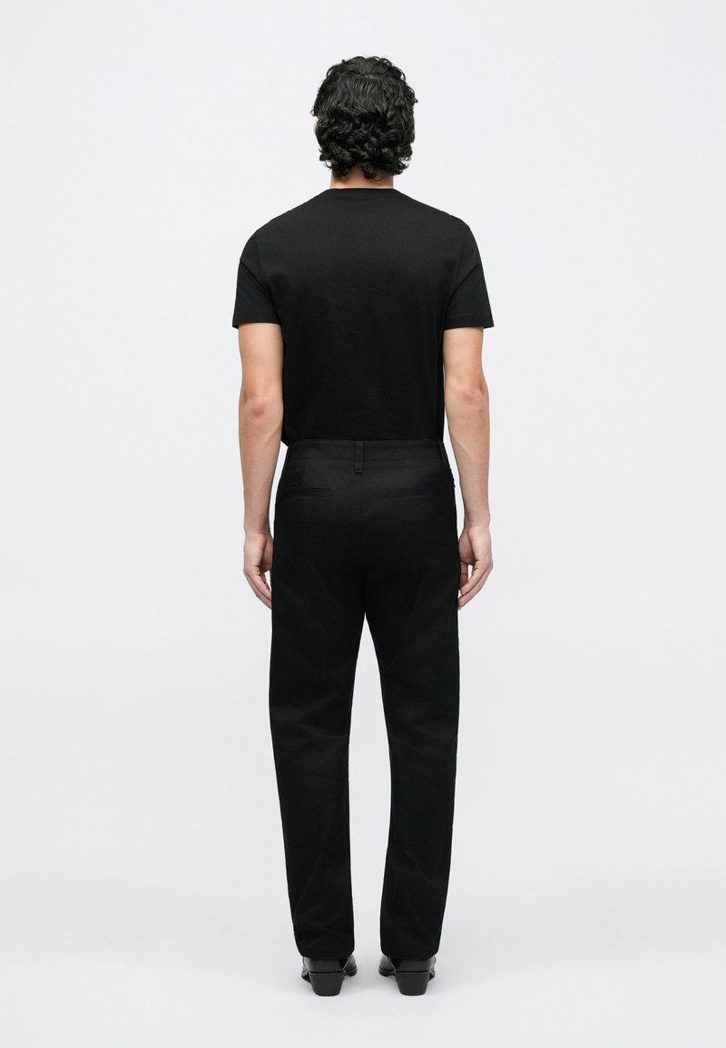 Svart t-shirt med korta ärmar och svarta byxor, sedd bakifrån. Tyget verkar slätt med en figurnära design och minimal detaljer.