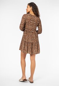 Braunes langärmliges Kleid mit floralem Muster, tailliert und mit rüschensaum. Das Muster zeigt kleine, bunte Blumen auf dem braunen Stoff.