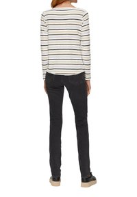 Langermige gestreepte top met crèmekleurige, gele, zwarte en grijze horizontale strepen, gecombineerd met zwarte skinny jeans en zwarte sneakers.