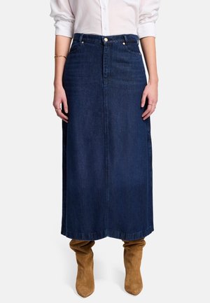 Jupe maxi en denim, bleu foncé, coupe droite, design à cinq poches, fermeture à boutons sur le devant, associée à des bottes beiges montantes.