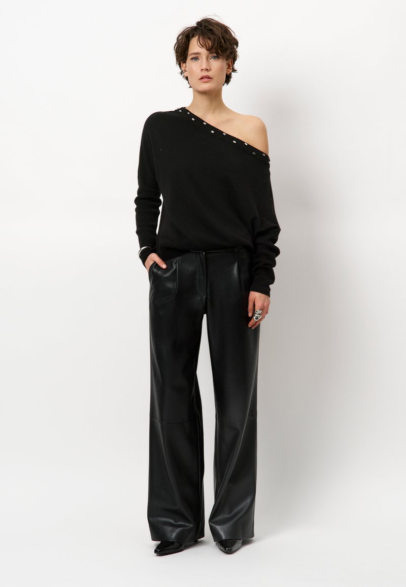 Schwarzer Off-Shoulder-Pullover mit silbernen Nieten entlang des Ausschnitts, kombiniert mit hoch taillierten schwarzen Leder-Hosen mit weitem Bein.