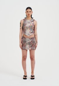 Conjunto de top corto y falda mini en una tela sintética brillante, con un estampado colorido de flores y dragones sobre un fondo de patrón de leopardo.