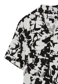 Camicia a maniche corte con motivo astratto bianco e nero, caratterizzata da una vestibilità rilassata, colletto e chiusura a bottoni. Tessuto texturizzato visibile.