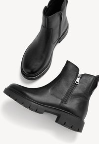 Schwarze Lederstiefeletten mit strukturiertem Finish, seitlichem Reißverschluss und robuster Gummisohle mit tiefen Profilmustern.