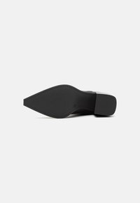 Suola di scarpa in pelle nera con forma appuntita. Finitura liscia, motivo di battistrada minimo e tacco a blocco solido per stabilità.