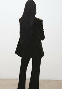 Traje de terciopelo verde oscuro con un blazer ajustado y pantalones de pierna ancha. La tela es suave con un ligero brillo, y el diseño presenta una silueta estructurada.