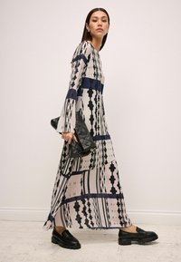 Robe longue et fluide beige avec des rayures noires et une bande bleue. Associée à des mocassins noirs et un sac à main noir texturé.