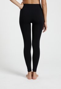 Leggings negros con una cintura alta, fabricados en material elástico. El diseño es ajustado al cuerpo, con un acabado liso y texturizado.