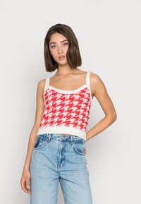 Top cropped com padrão xadrez vermelho e branco, com alças largas e textura felpuda, combinado com jeans de cintura alta em azul-claro.
