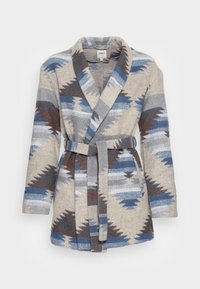 Bata beige con un patrón de zigzag multicolor en azul, gris y marrón. La tela parece suave, con un cinturón en la cintura y solapas anchas.