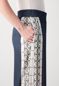 Navy blue elastic-waist pants feature a contrasting white panel with a geometric floral pattern in green and yellow, with side pockets.