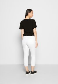 Top preto de manga curta com bainha rodada, combinado com calças brancas curtas. Modelo usa ténis pretos de camurça. Design simples e elegante.