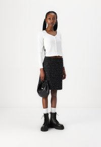 Haut à manches longues rayé blanc, jupe en tweed noir avec des éclats blancs, bottes de combat noires et un sac noir avec une poignée nouée.