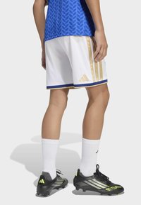 White athletic shorts with gold stripes and blue accents, paired with black soccer cleats featuring green highlights and white socks.