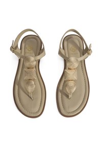 Beige sandalen met een platte zool, voorzien van drie getextureerde gouden accenten in verschillende vormen langs de band, waaronder ronde en vierkante ontwerpen.