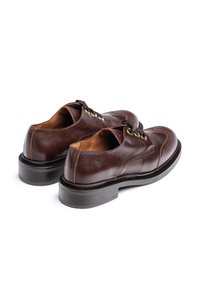 Bruine leren schoenen met een gepolijste afwerking, ronde neus en decoratieve stiksels. Beschikt over een zwarte zool en gouden oogjes voor de veters.