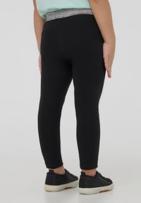 Leggings neri con una cintura elastica texturizzata in argento. Design aderente e orlo alla caviglia, indossati con sneakers nere.